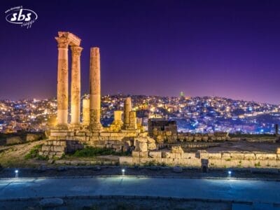 Le antiche colonne romane illuminate dominano il paesaggio urbano illuminato di notte ad Amman, in Giordania: una vista iconica da ammirare durante il tuo Gran Tour o viaggio completo.