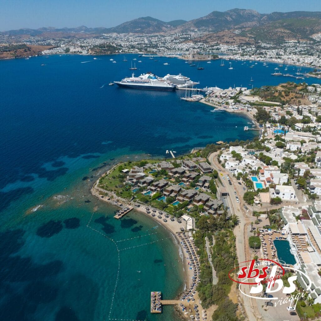 Vista aerea di una zona turistica costiera con spiagge, moli e hotel lungo il Mare, con navi da crociera attraccate in un porto turistico e montagne che si stagliano sullo sfondo: perfetta per un'esperienza indimenticabile al Tour Istanbulissima.