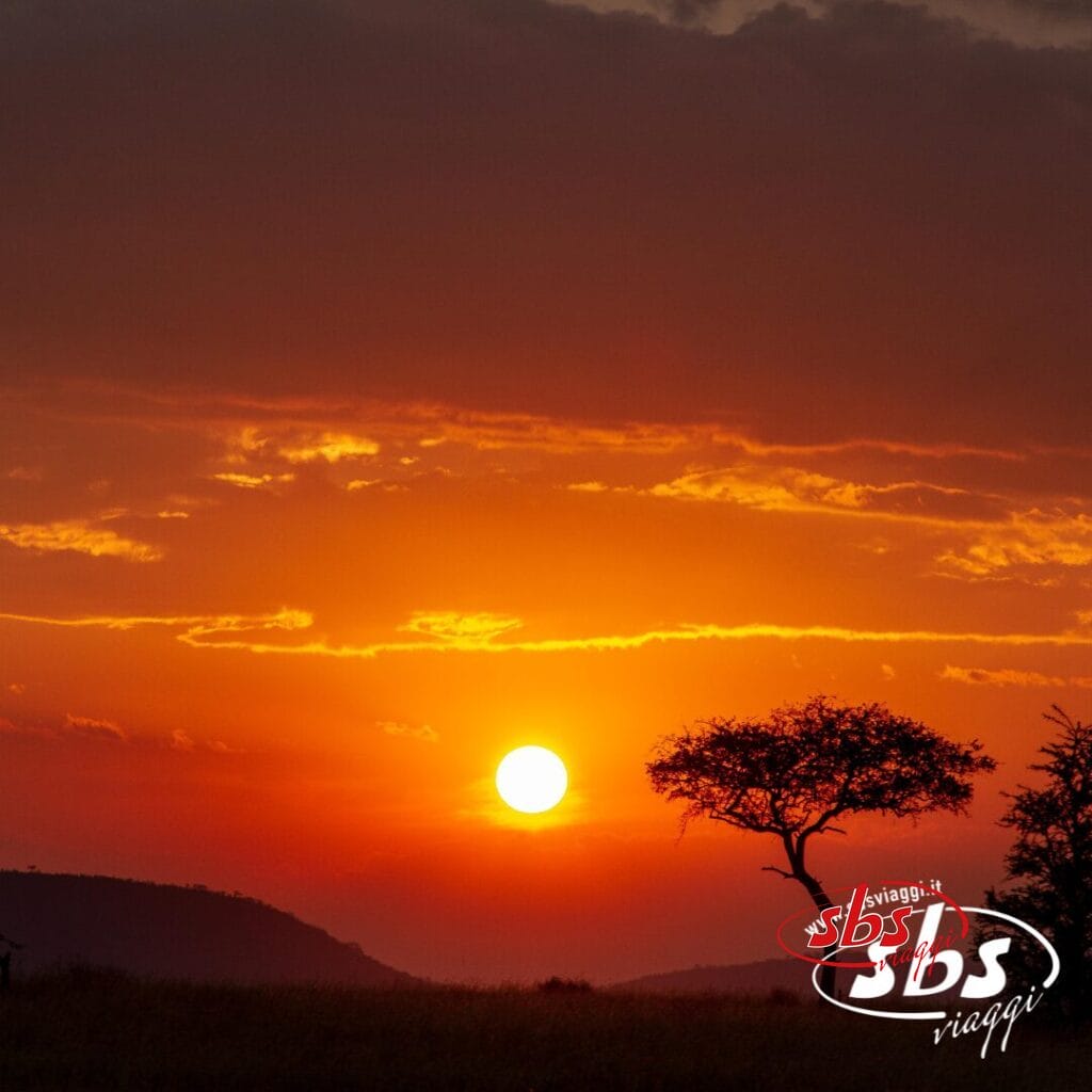 Tramonto arancione brillante su una savana africana con alberi e colline in silhouette, che cattura lo spirito di Discovery Kenya. Logo SBS Viaggi in un angolo.