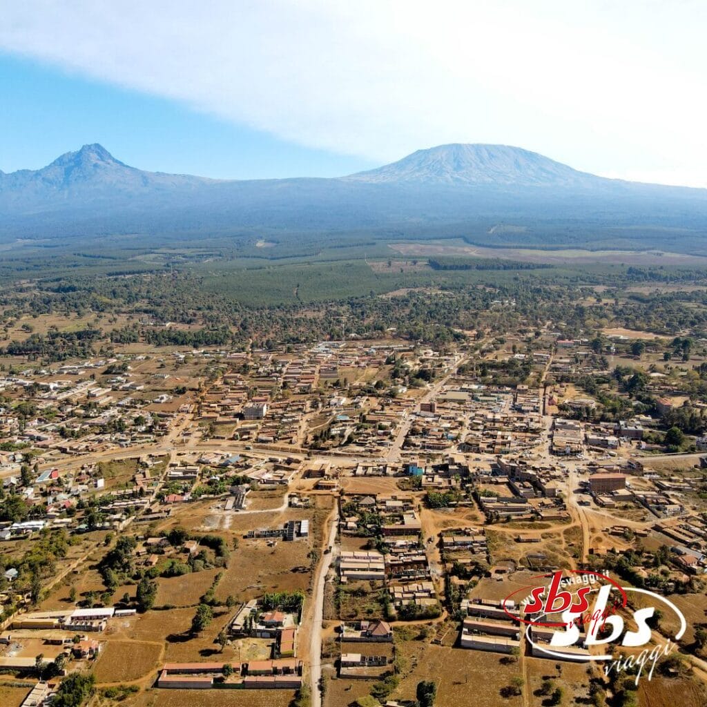 Vista aerea di una città del Kenya con edifici sparsi, campi e due grandi montagne sullo sfondo, tra cui il maestoso Kilimangiaro.
