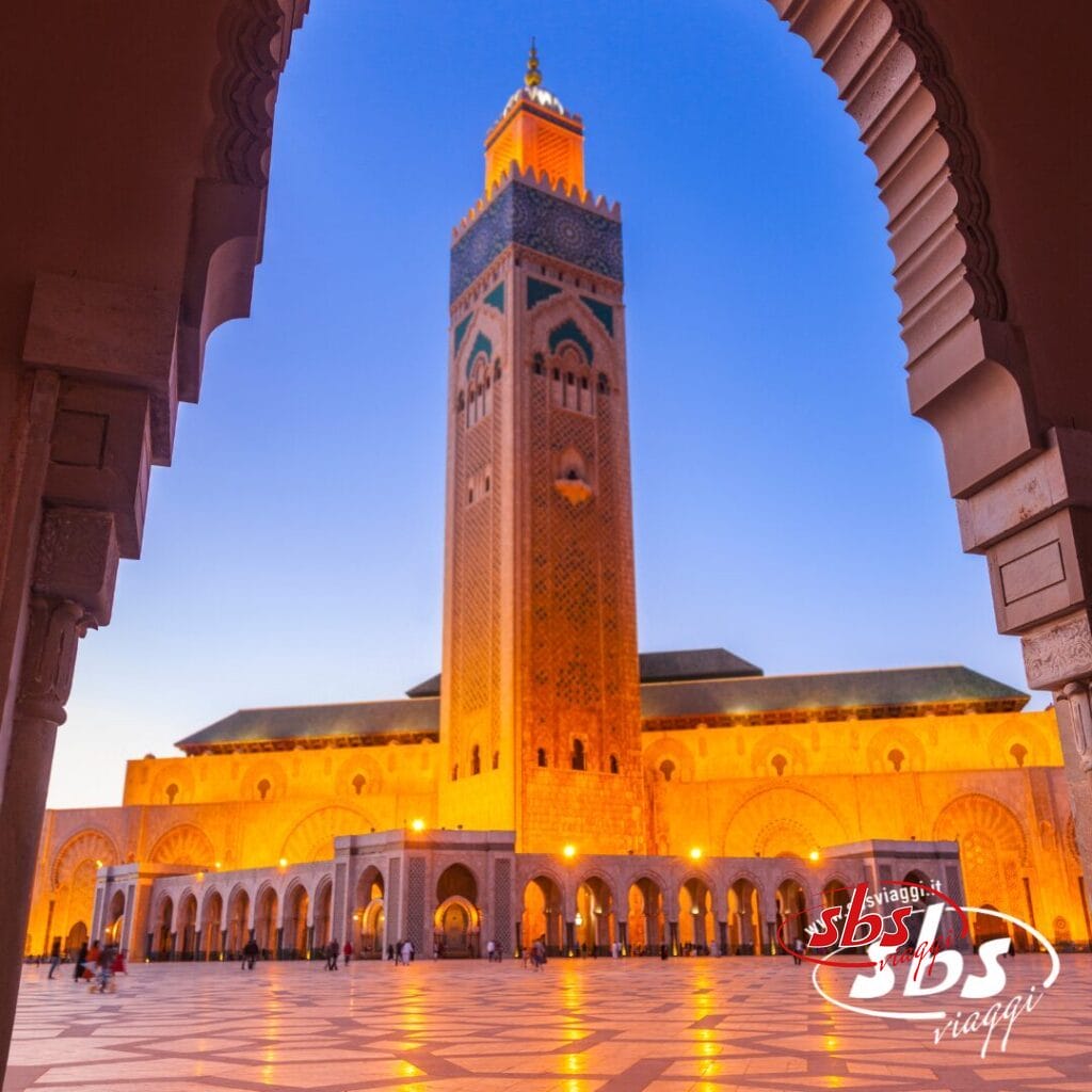 La moschea di Hassan II a Casablanca al tramonto, vista attraverso un arco, con una calda luce dorata: uno straordinario Panorama Marocchino che cattura la bellezza dell'architettura marocchina.