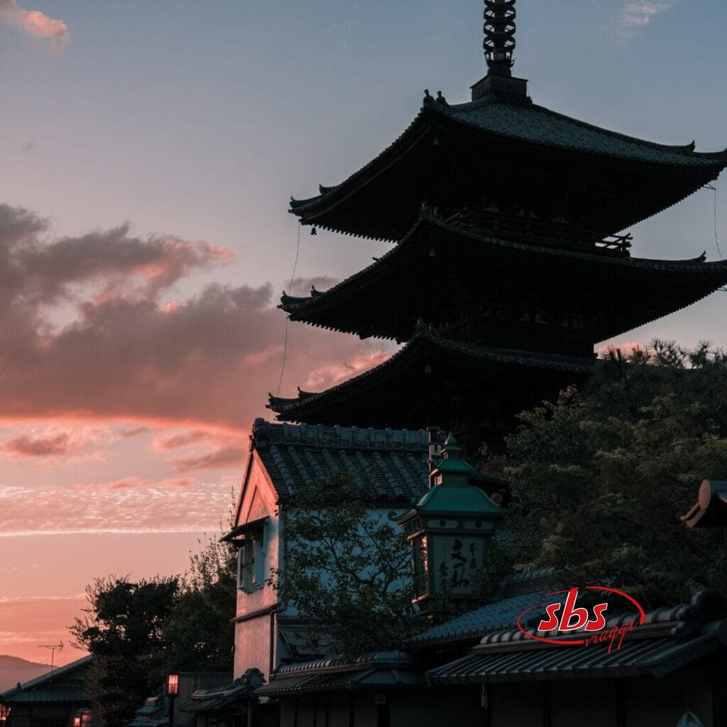 Una tradizionale pagoda giapponese che si staglia contro il cielo al tramonto, con tetti e alberi in primo piano, catturando la serena bellezza del Giappone, spesso apprezzata durante un Tour Giappone.