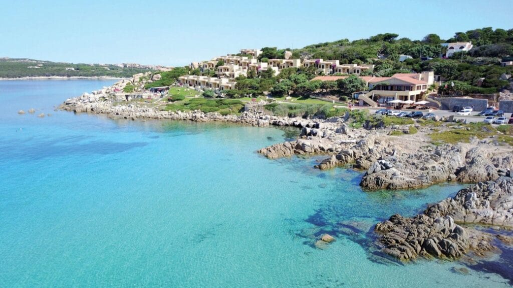 Costa rocciosa con acqua cristallina e case immerse nel verde nelle giornate di sole, creando uno scenario che ricorda un capolavoro di Bozza automatica.