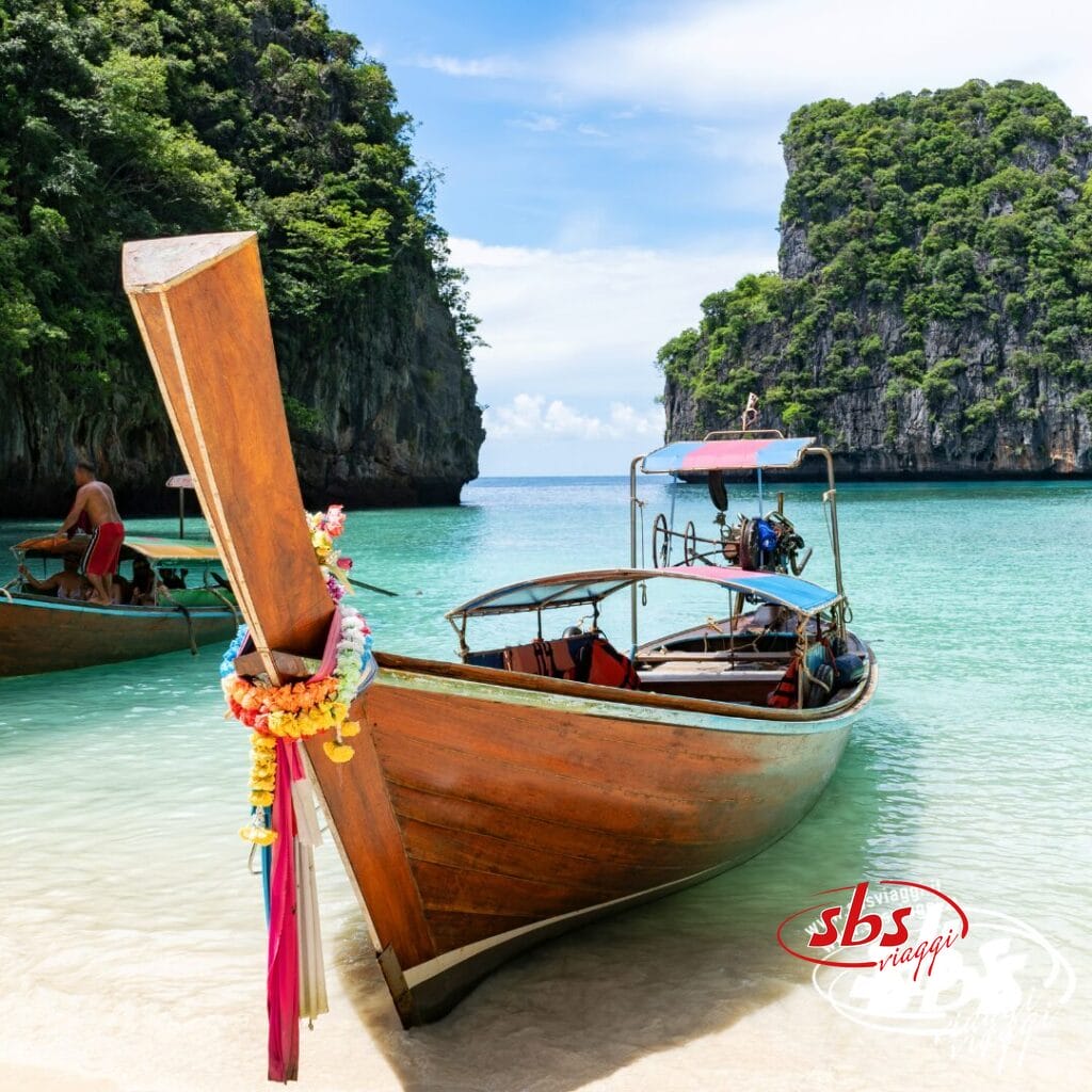 Una barca a coda lunga in legno su acque turchesi e cristalline, con scogliere e vegetazione lussureggiante sullo sfondo: uno scenario iconico di Phuket, perfetto per la tua avventura Estensione Mare Phuket o Tour Thailandia.