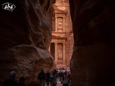 I turisti in tour attraversano uno stretto canyon verso l'antico Tesoro di Petra, in Giordania, scoprendo una delle meraviglie del mondo sotto una tenue luce del sole.