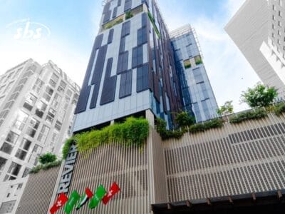 Moderno edificio alto con Bozza automatica, caratterizzato da vegetazione e bandiere sulla facciata, visto da un'angolazione bassa contro il cielo.