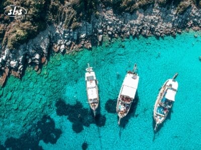 Vista aerea di tre caicchi ancorati in acque turchesi e cristalline, vicino a una costa rocciosa con vegetazione lussureggiante, perfetta per un'avventura Tour Istanbulissima.