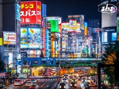 Strada trafficata di notte a Tokyo, in Giappone, illuminata da insegne al neon e cartelloni pubblicitari, con traffico intenso. Vivi la vivace vita notturna mentre programmi la tua avventura Foliage 2025 in questa dinamica città.