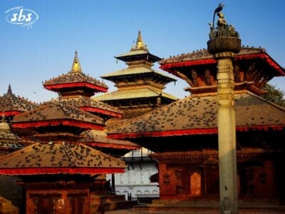 Un gruppo di templi tradizionali nepalesi in stile pagoda con tetti decorati, ricoperti di piccioni, che si stagliano contro un cielo azzurro limpido nella piazza Durbar di Kathmandu: una tappa obbligata di qualsiasi tour in Nepal o itinerario del Triangolo d'Oro.
