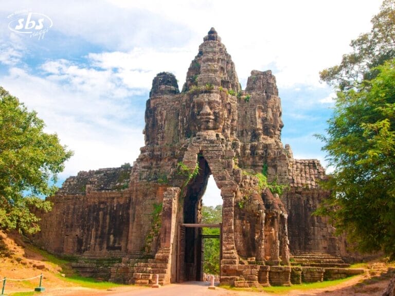 Antica porta in pietra con grandi volti scolpiti ad Angkor Thom in Cambogia, circondata da alberi e sotto un cielo parzialmente nuvoloso: una tappa obbligata di qualsiasi tour Grantour o in Cambogia.