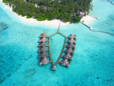 Vista aerea di bungalow sull'acqua che si estendono su un'isola tropicale delle Maldive, con una spiaggia di sabbia bianca, acque turchesi e lussureggianti alberi verdi: perfetti per un tour indimenticabile.