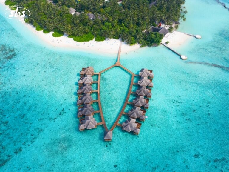 Vista aerea di bungalow sull'acqua che si estendono su un'isola tropicale delle Maldive, con una spiaggia di sabbia bianca, acque turchesi e lussureggianti alberi verdi: perfetti per un tour indimenticabile.