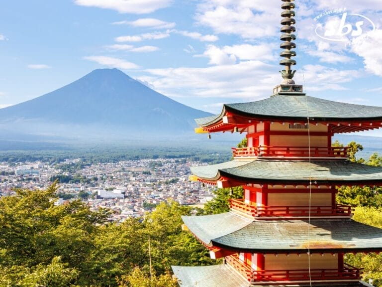 Una pagoda rossa si erge in primo piano, con il Monte Fuji e un paesaggio urbano visibile sullo sfondo sotto un cielo parzialmente nuvoloso, catturando la serena bellezza del Giappone durante la stagione dei Matsuri.