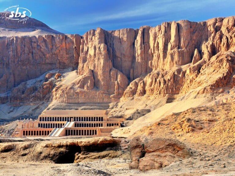 Antico tempio con colonne incastonate nelle pareti rocciose sotto un cielo azzurro in un paesaggio desertico, che ricorda la Valle dei Re vicino al Cairo: una tappa obbligata di qualsiasi tour in Egitto.