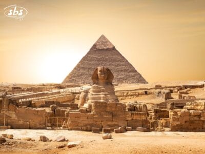 La Sfinge e una piramide al tramonto nel deserto egiziano con un cielo dorato sullo sfondo, catturano il fascino senza tempo del Cairo ed evocano sogni di una Crociera sul Nilo verso Abu Simbel.
