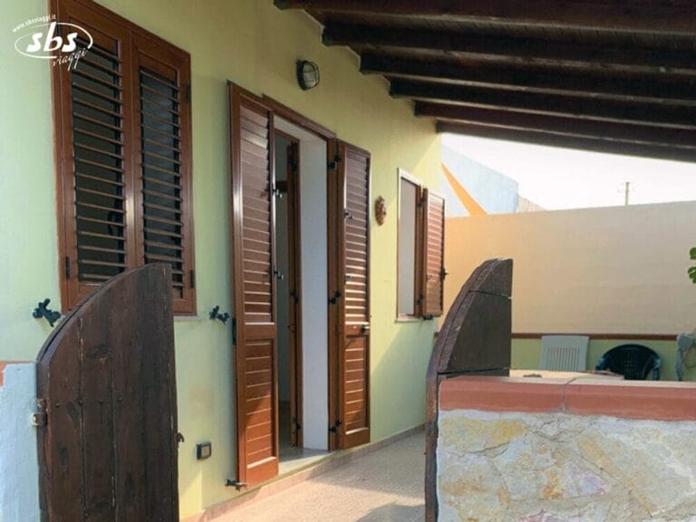 Il patio del Residence Il Villaggio del Mago è dotato di persiane in legno, porte e un muro parziale in pietra sotto un tetto con travi in legno.