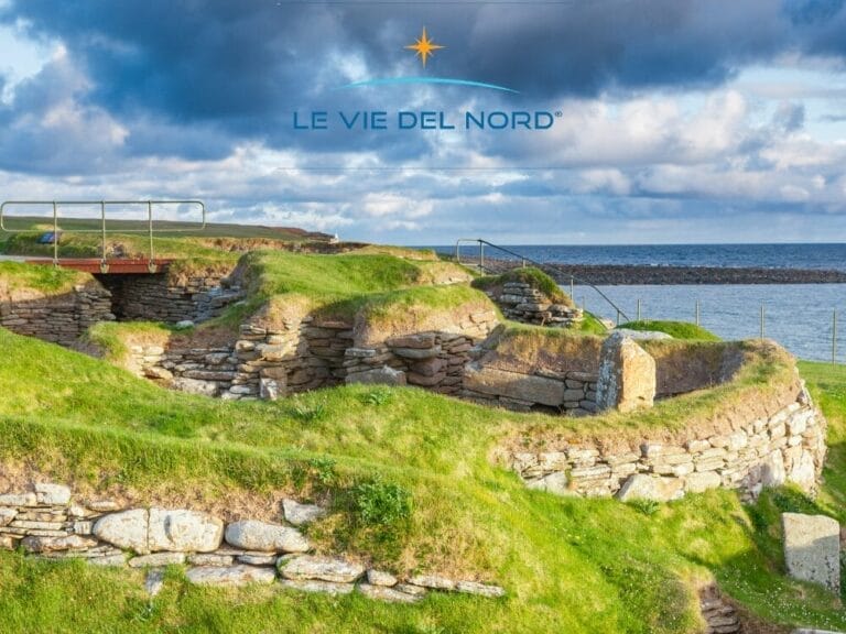 Antiche rovine in pietra sulle colline erbose degli Altipiani in riva al mare, sotto un cielo nuvoloso, con la scritta "Le Vie Del Nord" in alto: perfetto per un Tour Scozia o per esplorare le Isole Orcadi.