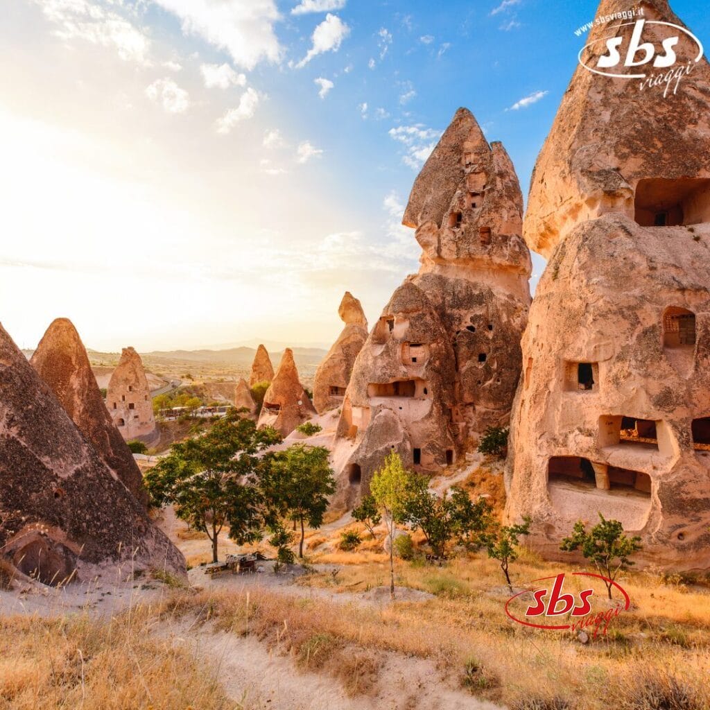 Camini delle fate e antiche abitazioni rupestri in Cappadocia, Turchia, al tramonto, con alberi sparsi in primo piano: una tappa obbligata di qualsiasi Tour della Turchia o di un'esperienza di Tour dalla Bari.