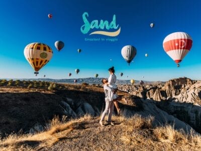 Una coppia si abbraccia su una scogliera con mongolfiere colorate che fluttuano nel cielo sopra di loro, catturando un momento senza tempo come una Bozza automatica.