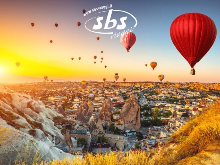 Mongolfiere sorvolano un paesaggio roccioso e una città al sorgere del sole; il logo "sbs viaggi" appare nel cielo, evidenziando un Tour della Turchia indimenticabile.